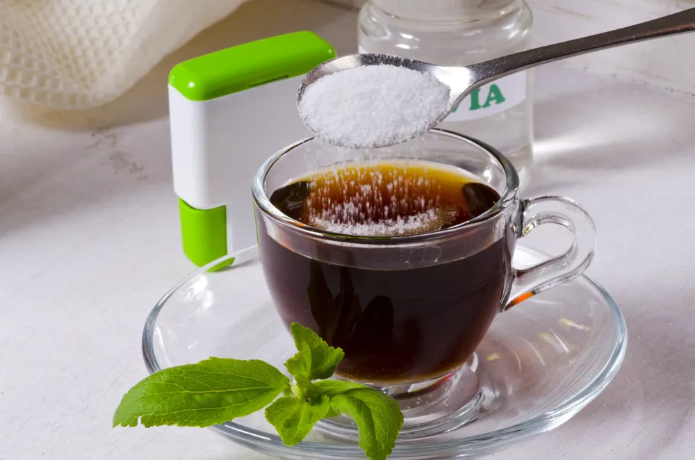 Granulated sweetener being spooned into a cup of black tea